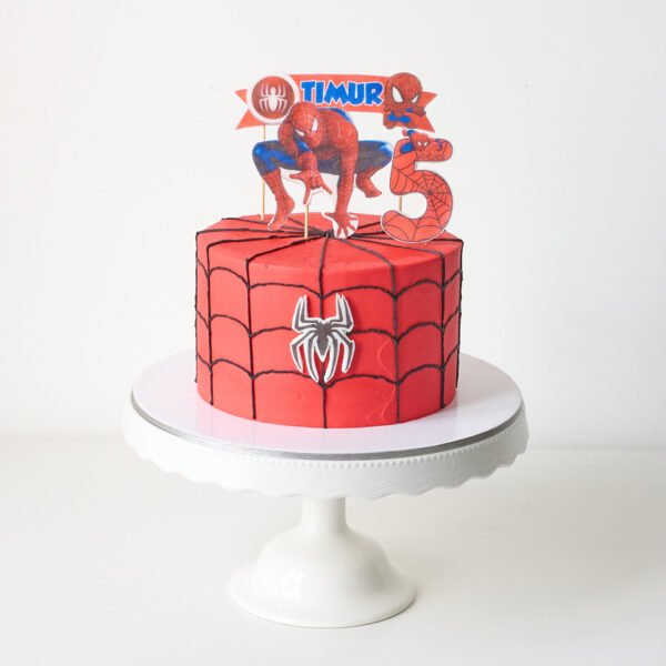 Torta circular cubierta de chocolate con decoración comestible de la cara de Spiderman y redes.